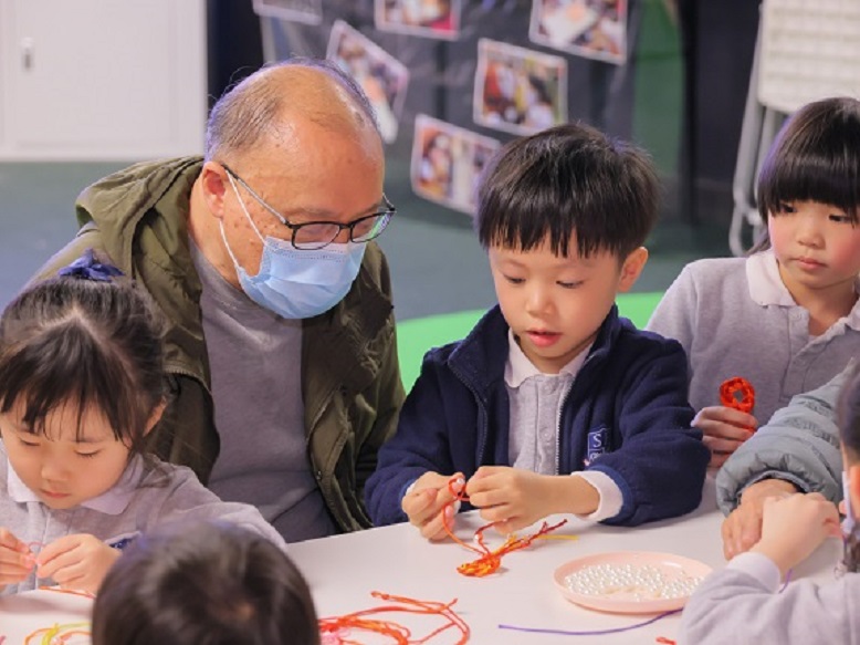 小朋友教长者们用黄、红色的绳子穿珠做“新春如意结”，大家都十分投入。
