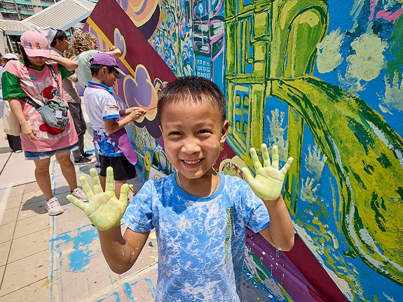 Children, volunteers and neighbours happily paint a mural together.