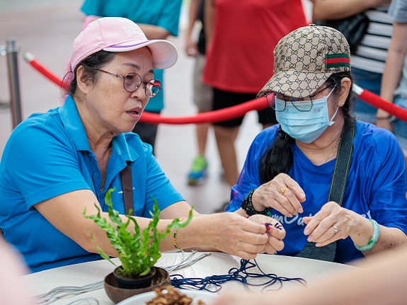 林女士（左）向另一位长者展示如何将绳子打结来吊挂椰壳花盆。 
