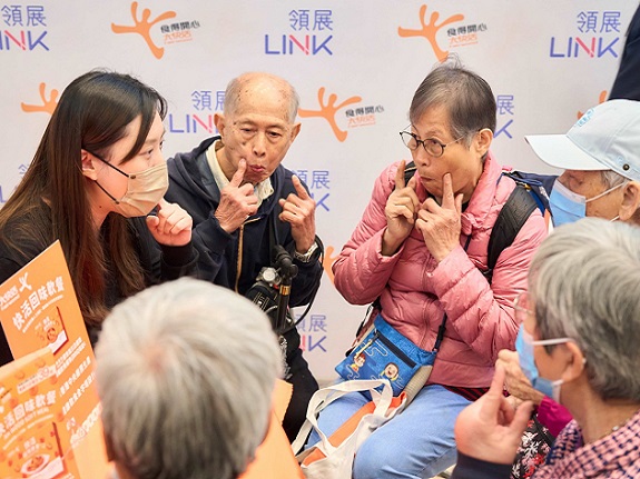 A group of elderly residents gather around the Mobile Swallowing Assessment Booth’s consultation table, attentively listening to explanations about dysphagia and its management.